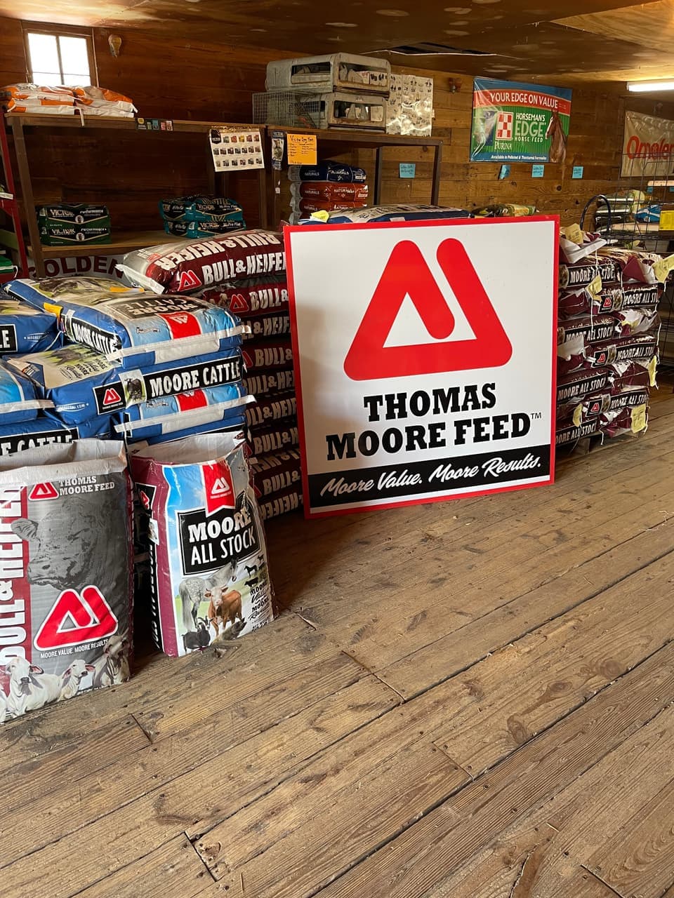 Moore Cattle, Bull & Heifer, and Moore All Stock cattle feed bags under the Thomas Moore Feed sign on the sales floor at Mustang Creek Feed Seed & Supply in Rio Vista, Texas